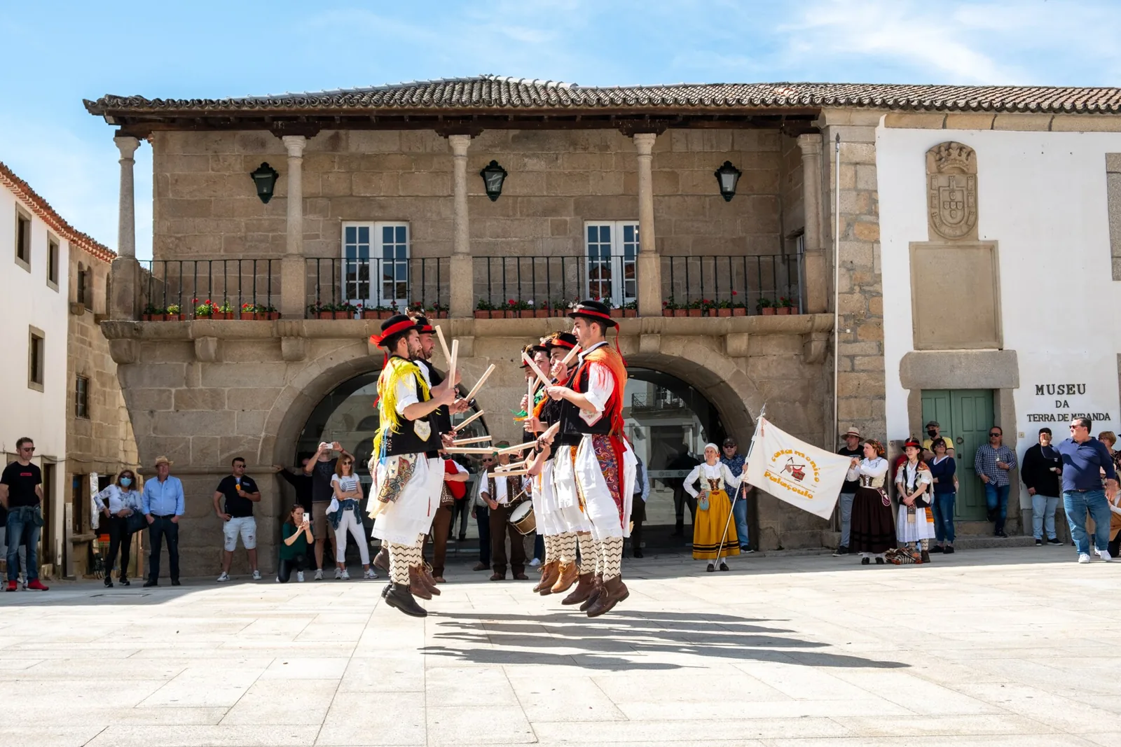 Grupo de pauliteiros de Palaçoulo em dança de paus diante de um edifício de arcadas