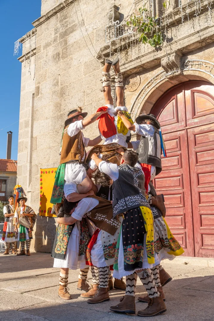 Grupo de pauliteiros de Sendim com trajes coloridos junto ao portal de uma igreja