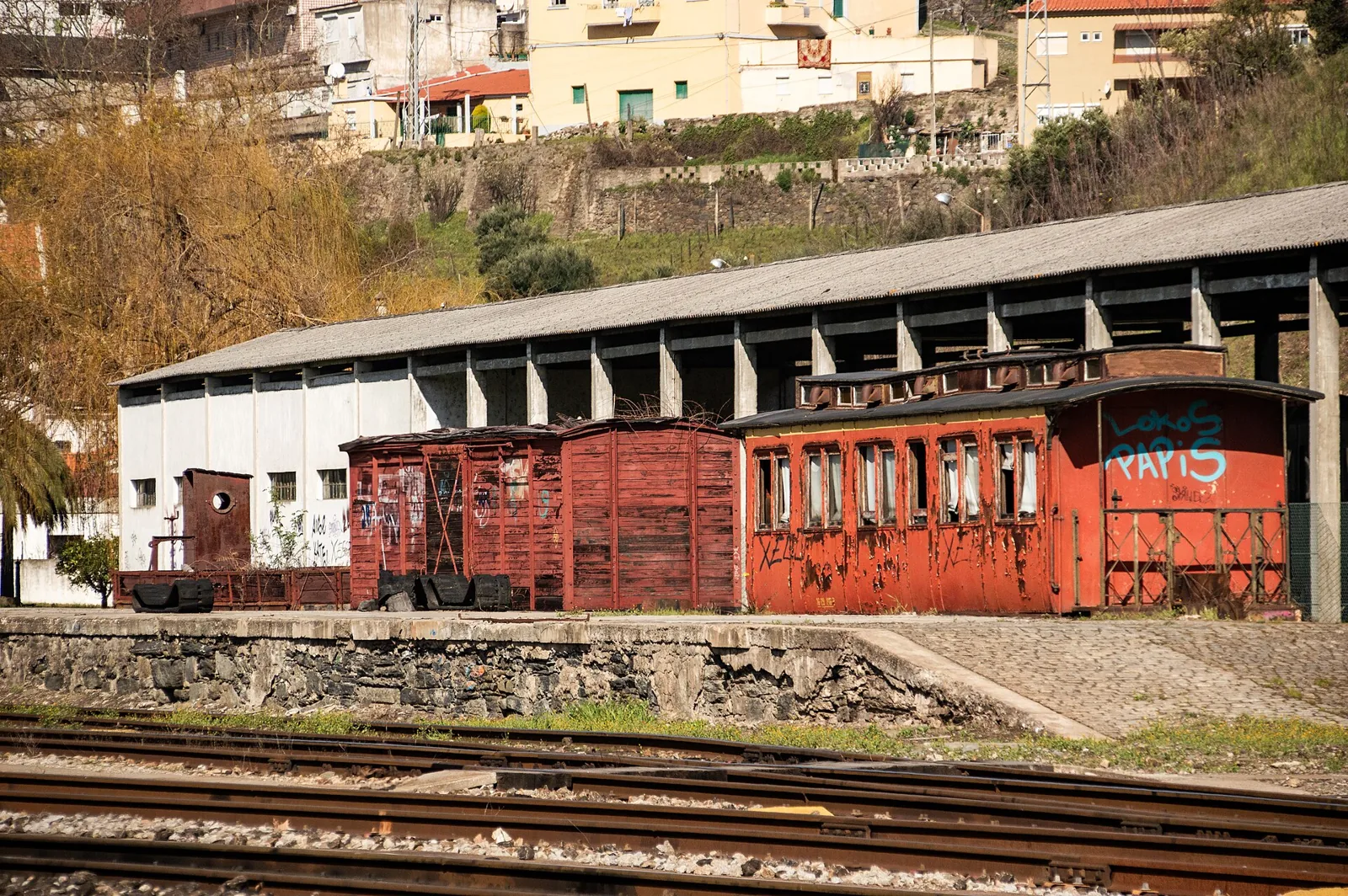 Barracão e velhas carruagens de madeira pintadas de vermelho, junto às linhas da Estação da Régua