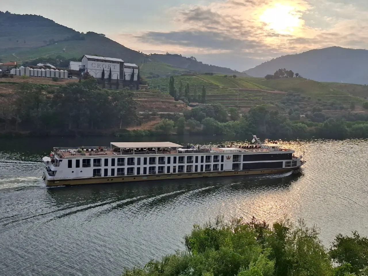 Barco de cruzeiro no rio Douro ao pôr do sol, enquadrado pelas encostas de vinha do vale
